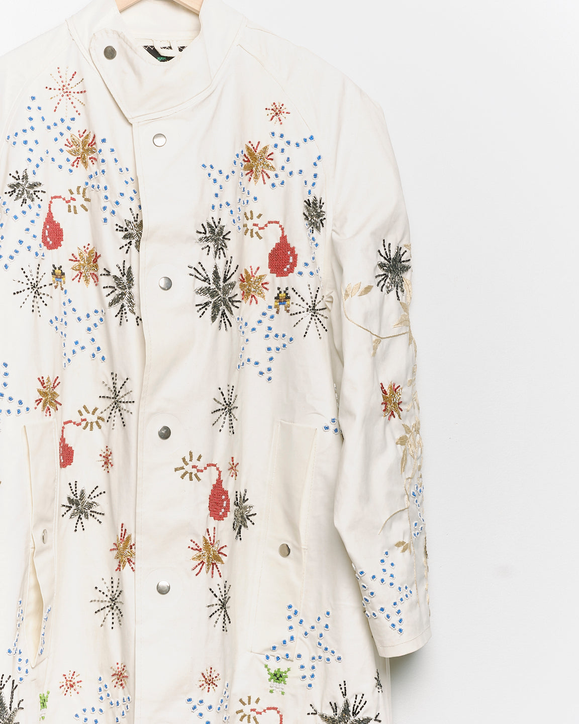 Long reworked white coat with embroidered motifs, close up view. 
