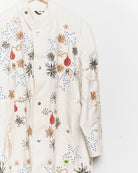 Long reworked white coat with embroidered motifs, close up view. 