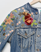 Vintage denim jacket with embroidery and tufted motifs, close up view. 