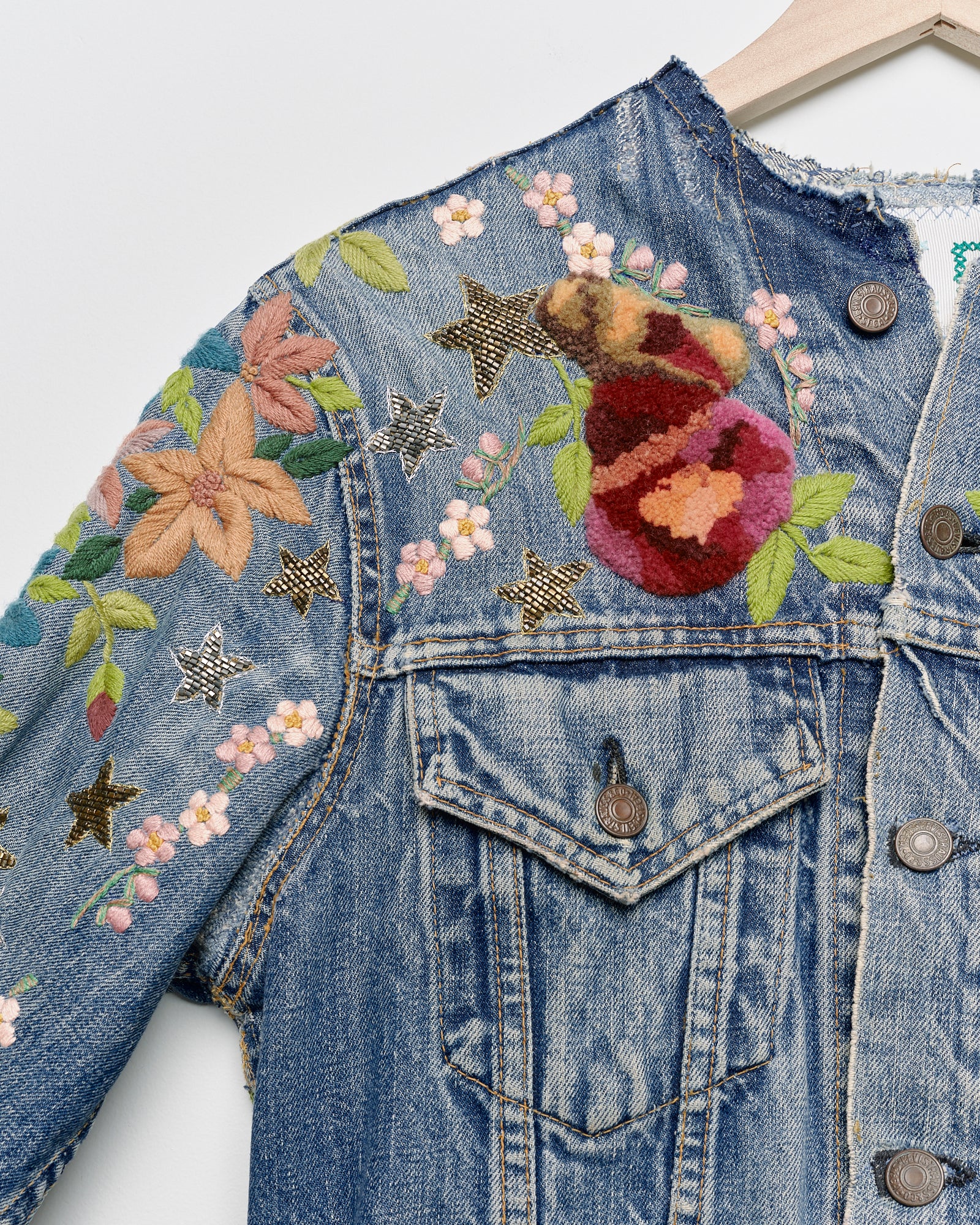 Vintage denim jacket with embroidery and tufted motifs, close up view. 