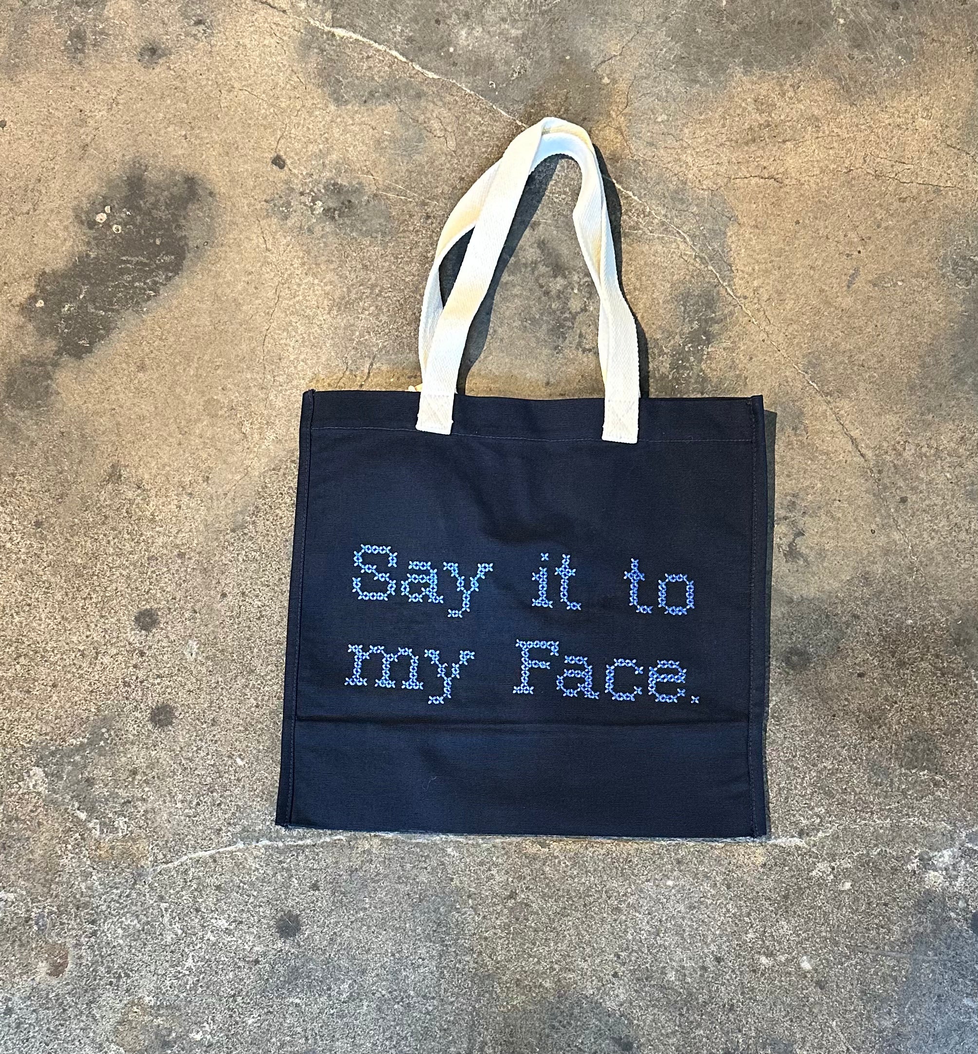 Bag with “Say it to my face” embroidered in cross stitch, front view.