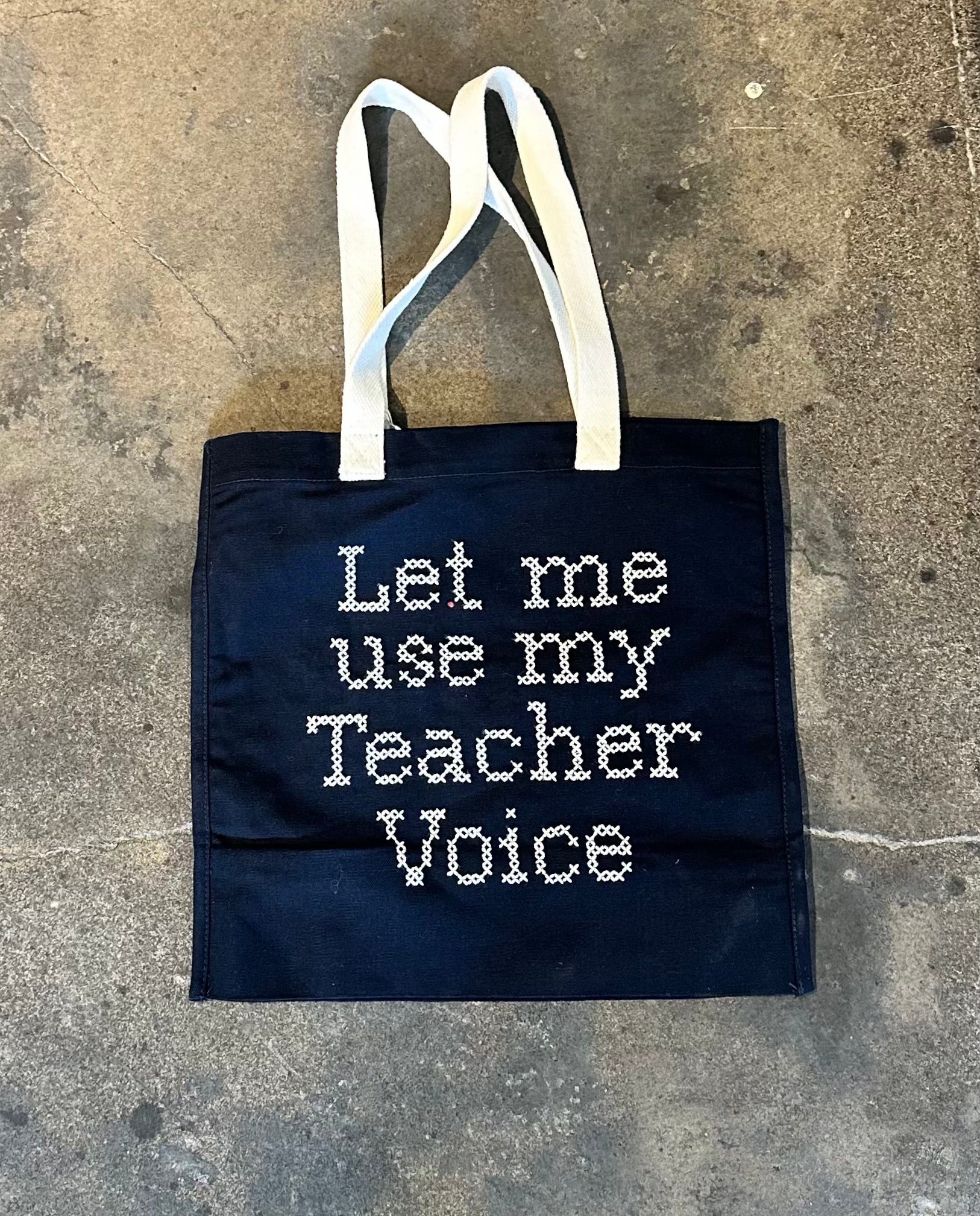 Bag with “Let me use my teacher voice” embroidered in cross stitch, front view.