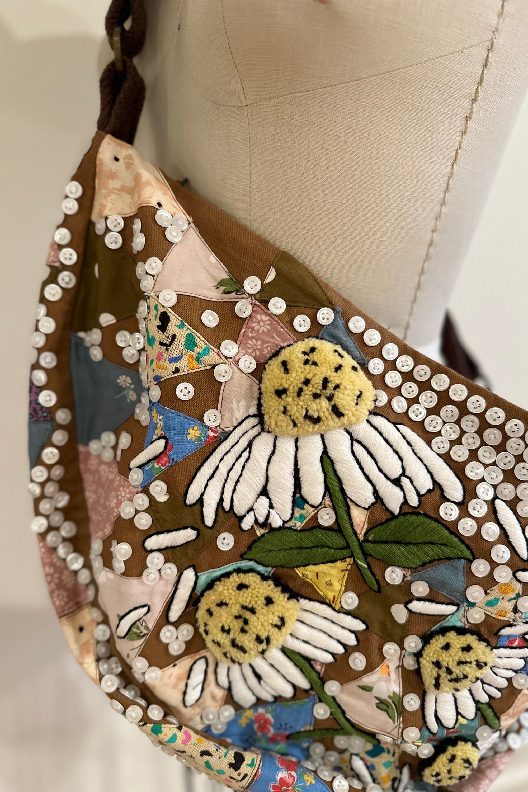Sling bag with embroidered and button embellishments, close up view